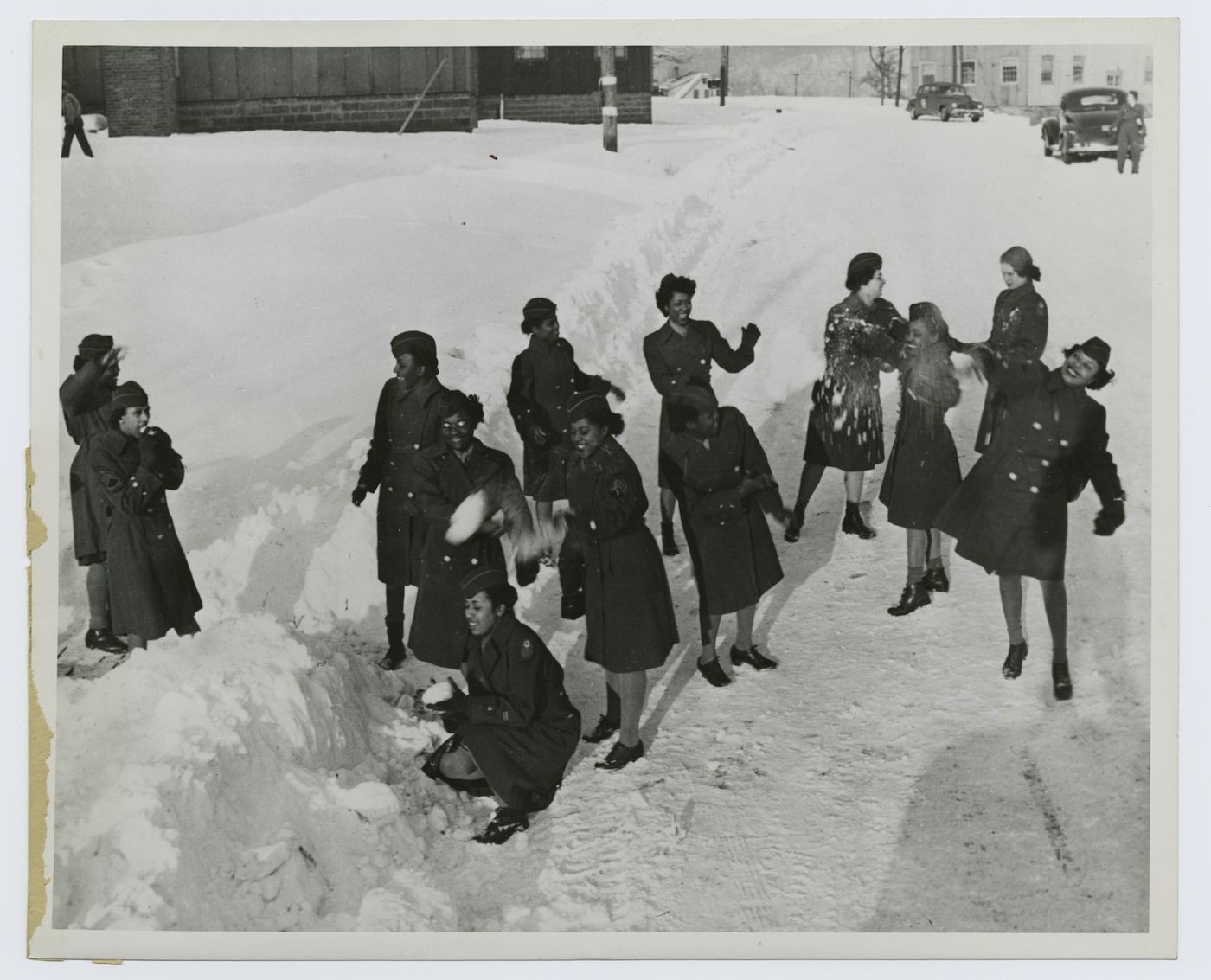 A black and white photograph of a group of women having a snowball fight in a snow-covered street.