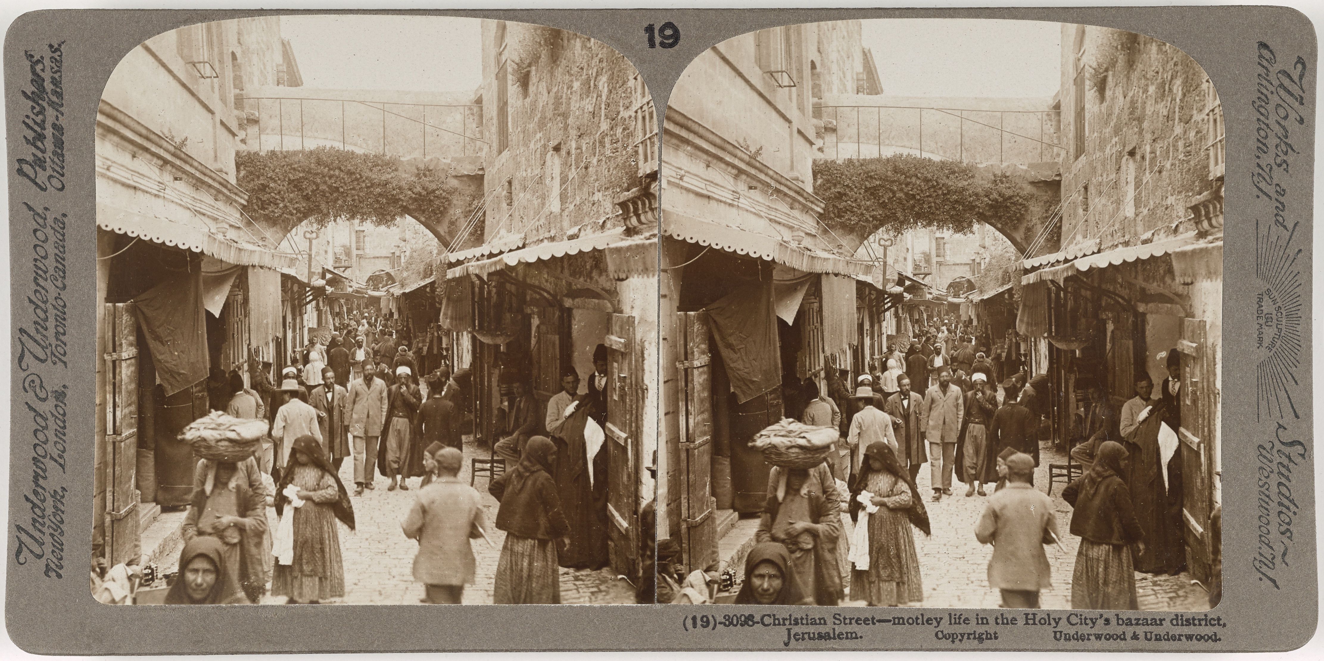 A vintage sepia-toned stereoscope image of a bustling street scene in the Holy City's bazaar district of Jerusalem, filled with people, vendors, and traditional architecture.