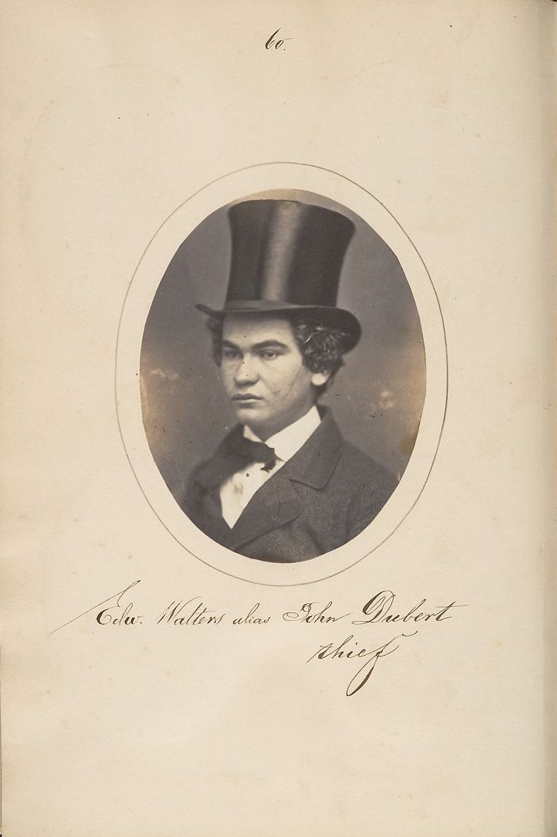 A sepia-toned oval portrait of a man in a top hat and suit, with handwritten text identifying him as 'Edu. Walters alias John Dubert' and 'thief'.