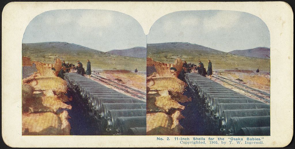 Stereoscopic photograph of a field filled with 11-inch artillery shells, with mountains in the background.