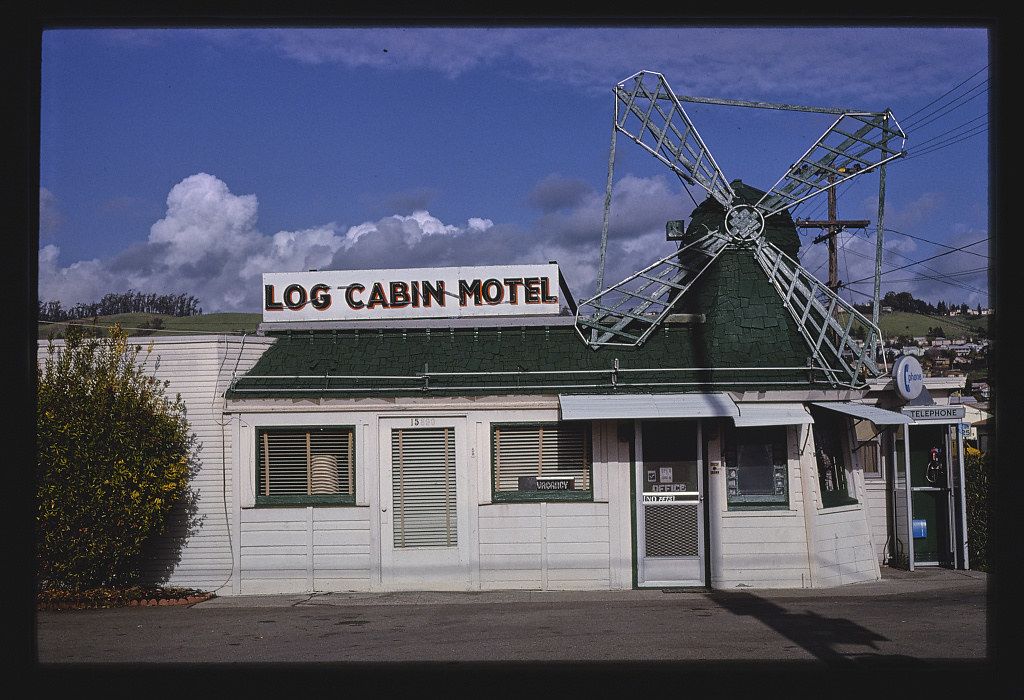 A vintage roadside motel with a windmill on the roof and a telephone booth.