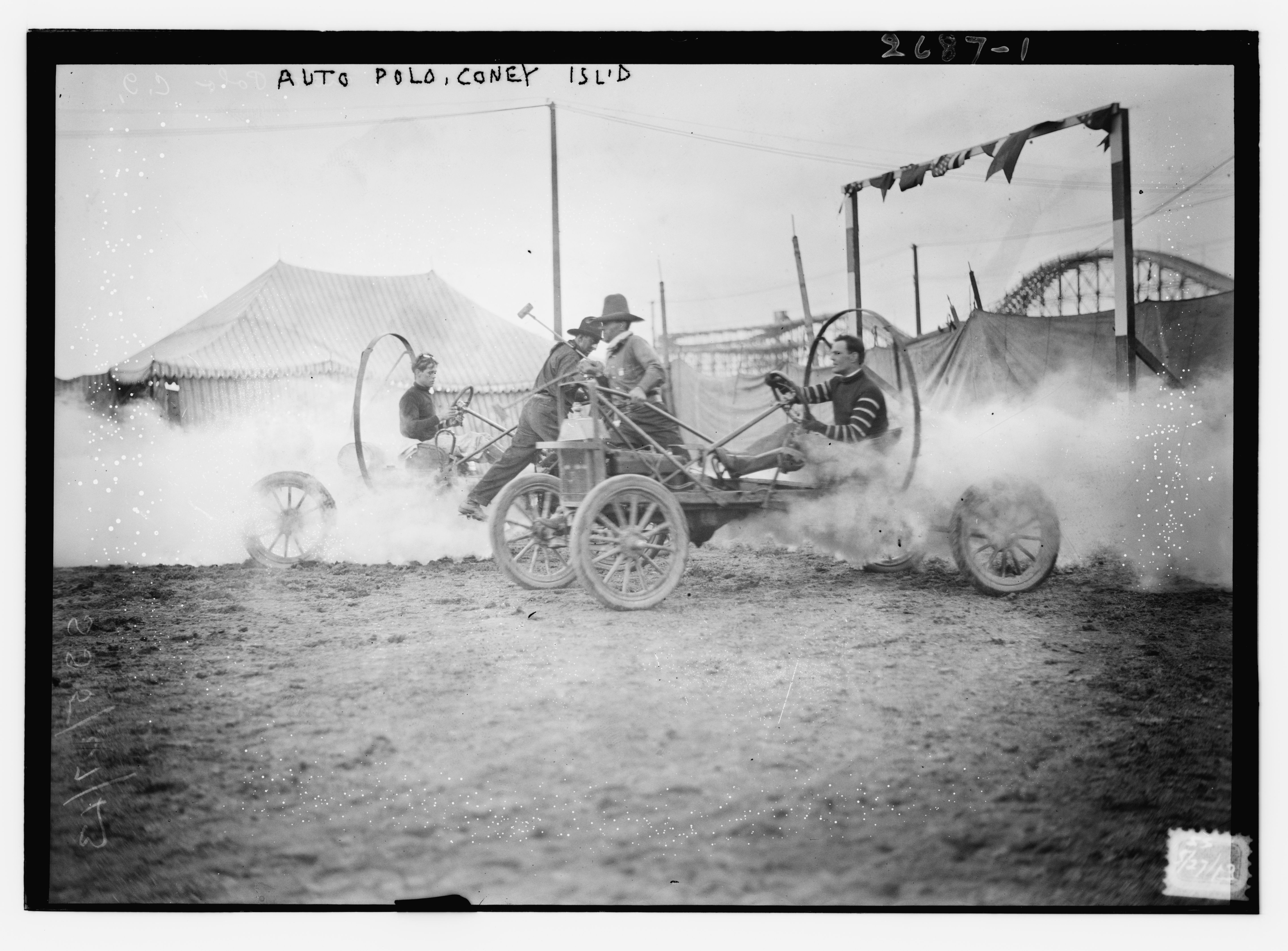 Black and white photograph of an auto polo match at Coney Island, showing two small vehicles with players wielding mallets, kicking up dust on a field with spectators and a tent in the background.