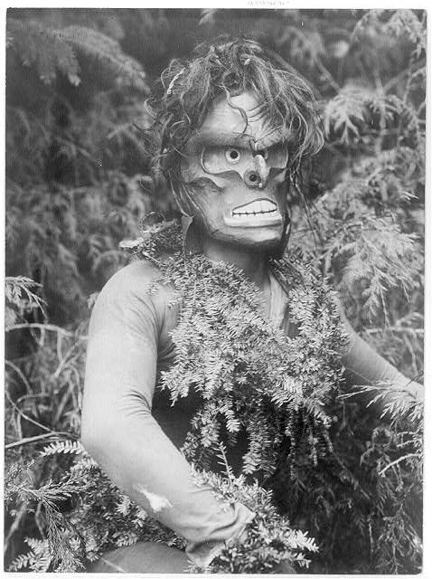 A black and white photograph of a person wearing a mask and foliage costume.