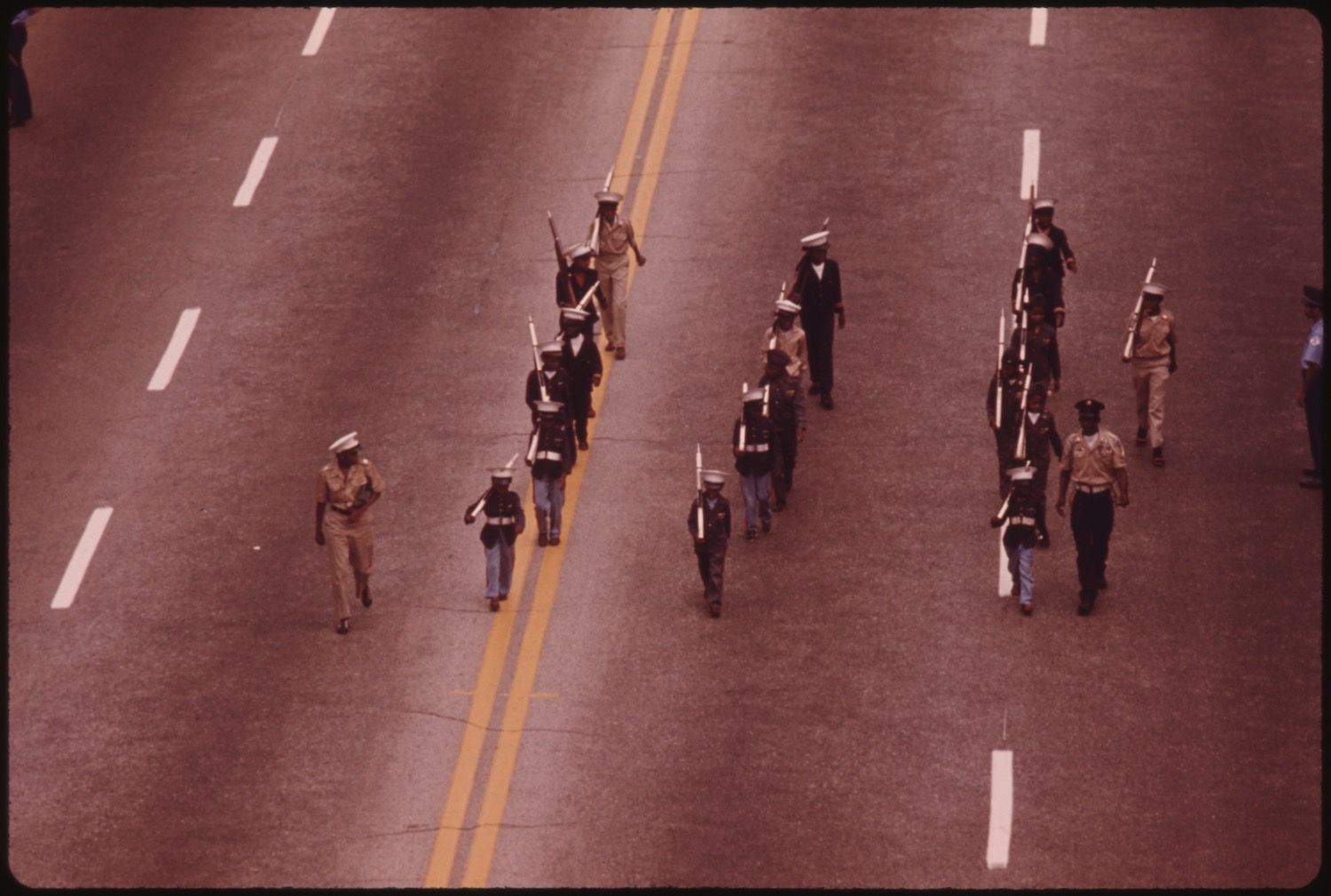 A high-angle view of a group of people in uniform marching down a road with lane markings.