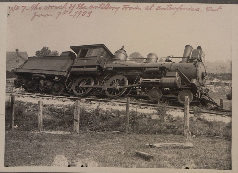 A vintage black and white photograph of a derailed train wreck in a grassy field, labeled 'No. 7 - The wreck of the artillery train at Enton, France, June 9th, 1903'.