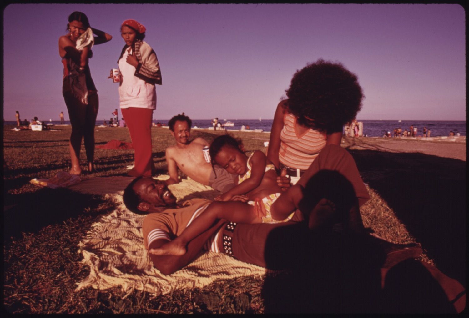A vintage photograph of a family enjoying a day at the beach, with a warm, pinkish-purple hue and a grainy texture.