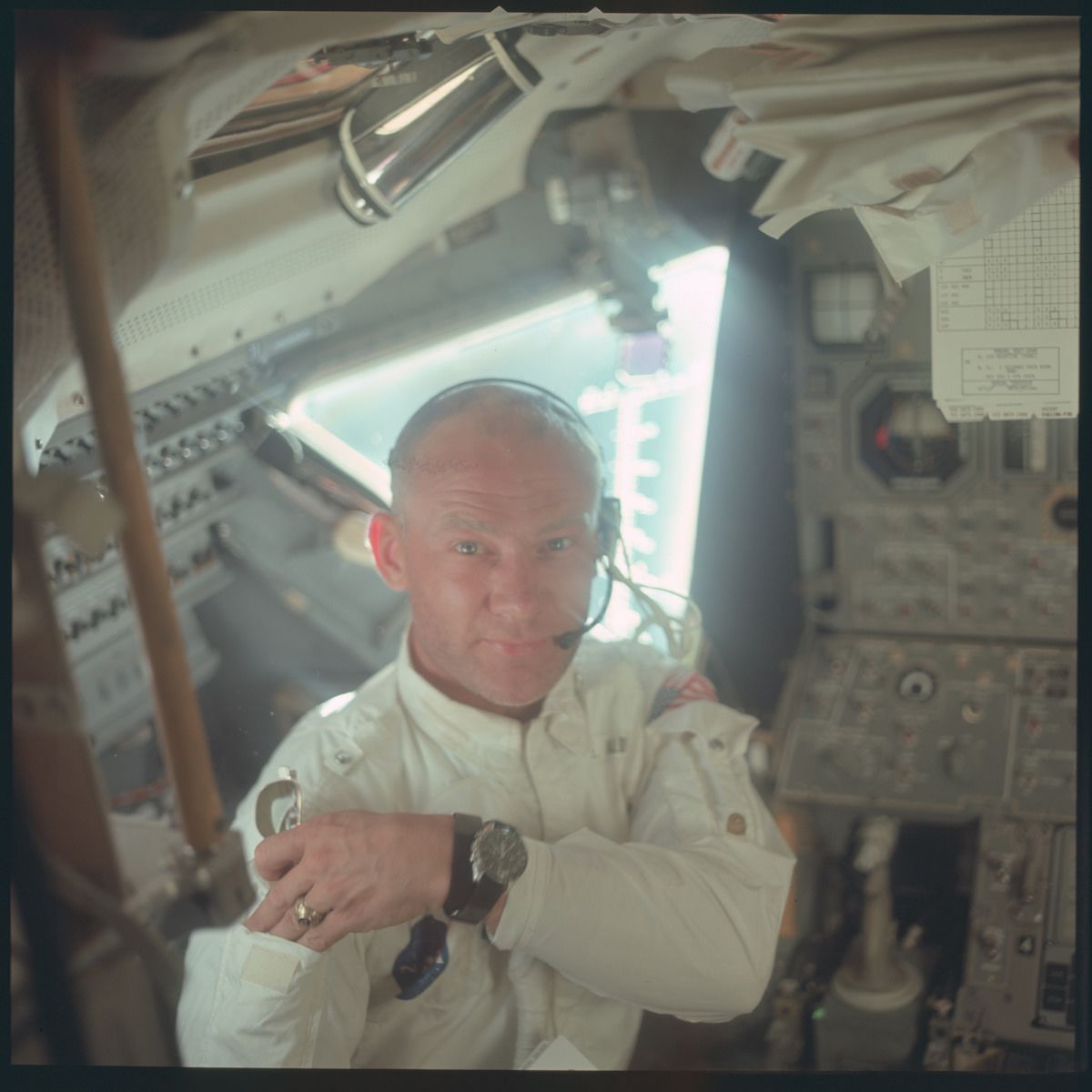 A close-up of an astronaut inside a spacecraft cockpit, looking at a watch on his wrist.