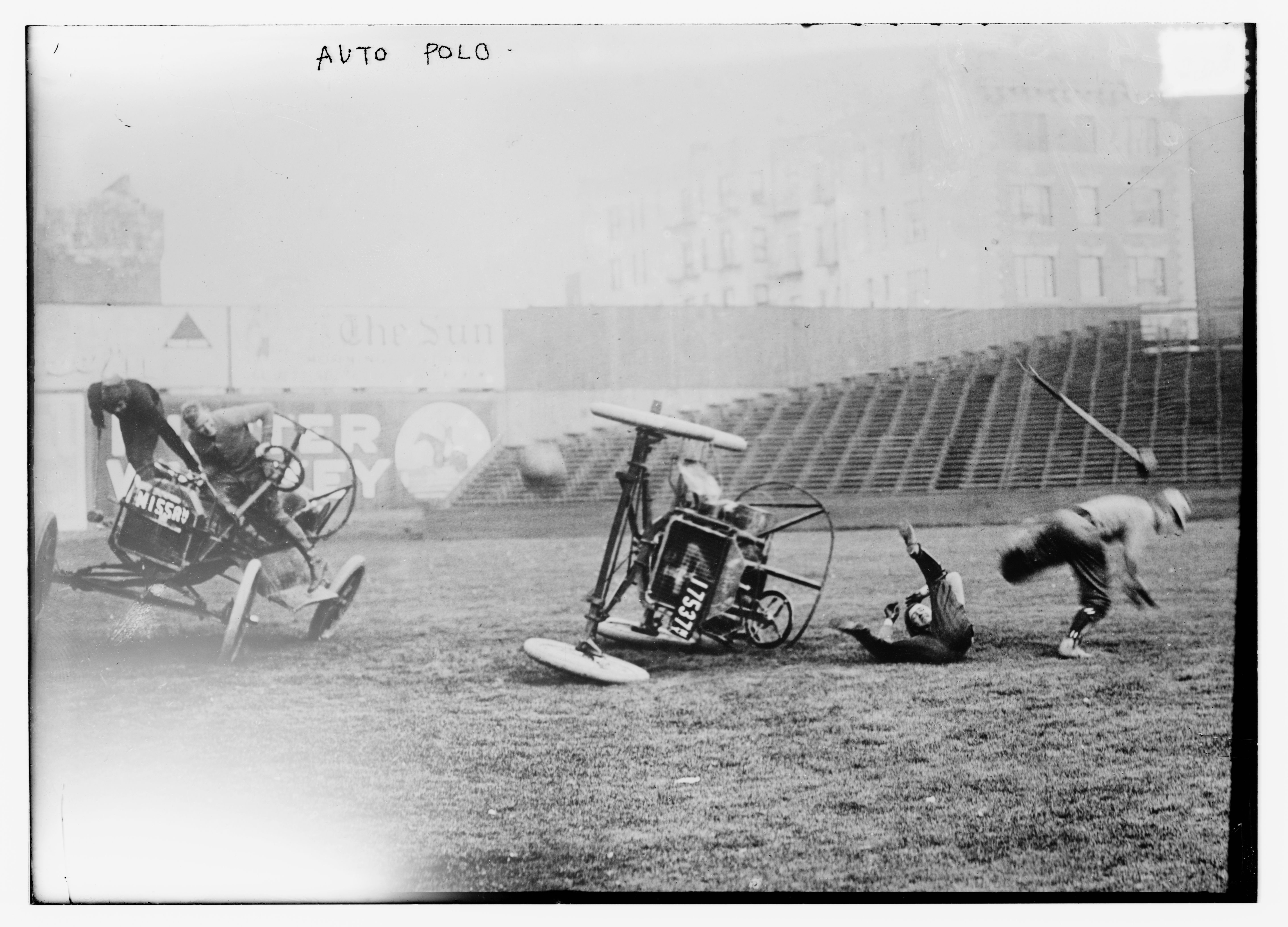 A vintage black and white photograph of an auto polo match with vehicles crashing and players falling on a grassy field.