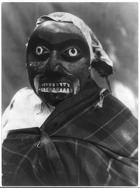 A black and white photograph of a person with a striking and somewhat unsettling painted face.