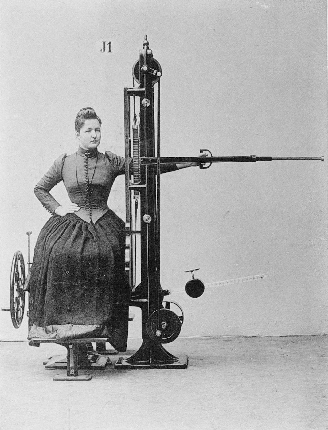 Vintage black and white photograph of a woman seated in a complex mechanical device.