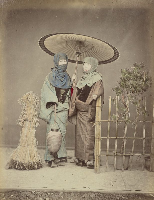 Vintage photograph of two Japanese women in traditional clothing standing under a large umbrella.