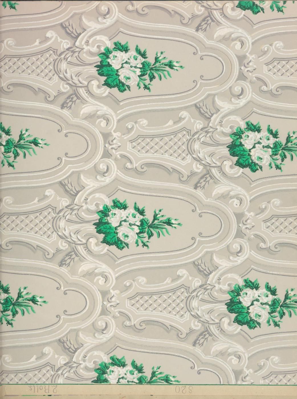Close-up of a vintage wallpaper with a beige background and a repeating pattern of ornate shapes, diamond lattices, and small green floral motifs.
