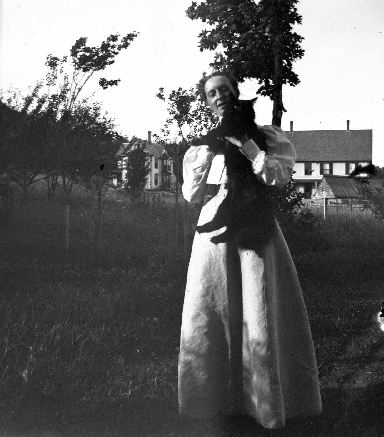 A vintage black and white photograph of a woman holding a cat in a field.