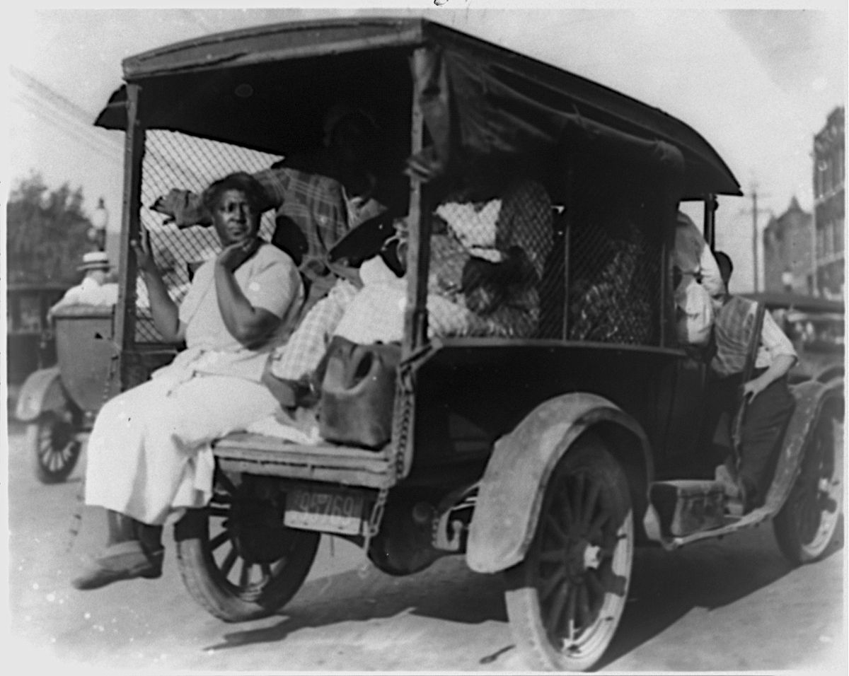 A black and white photograph of a group of African American individuals traveling in an open-top car.