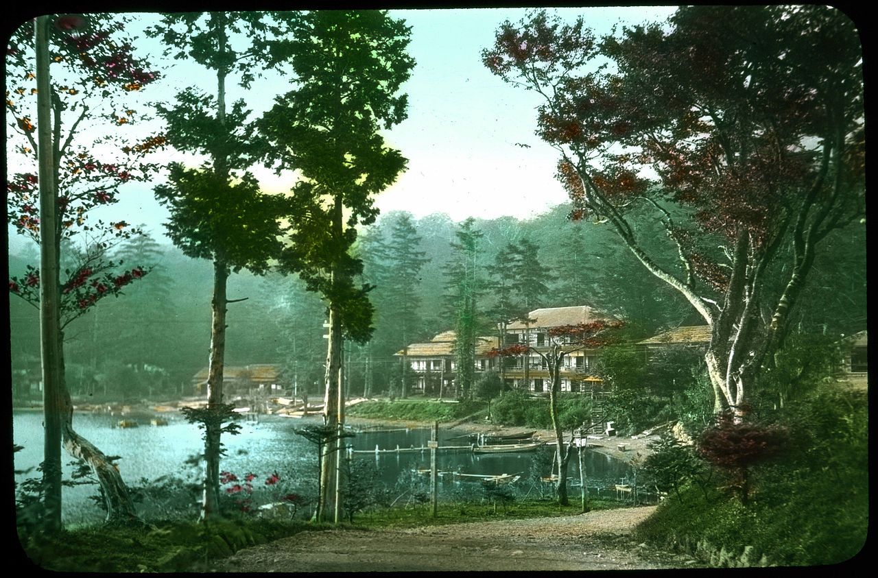 A vintage lakeside scene with wooden buildings, a dock, and lush vegetation.
