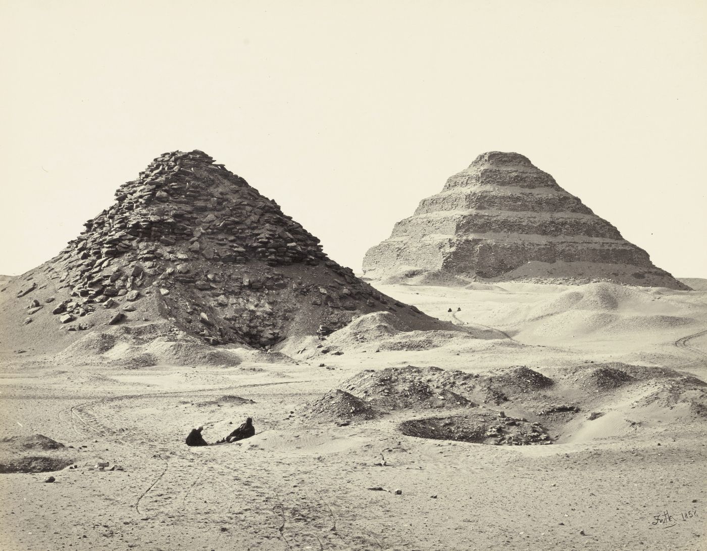 Sepia-toned photograph of two pyramids in a desert landscape.