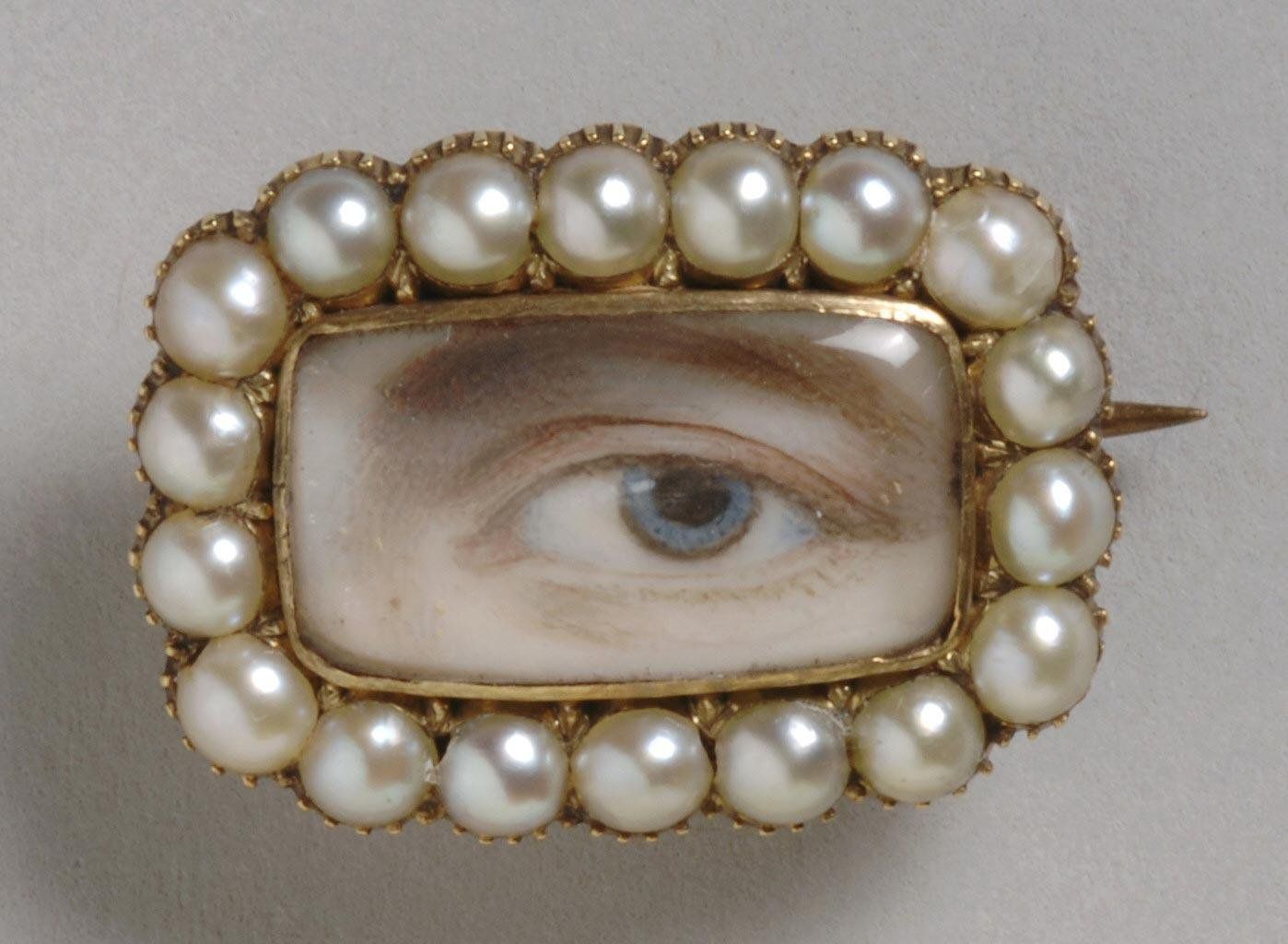 Close-up of a vintage brooch with a painted eye surrounded by pearls.