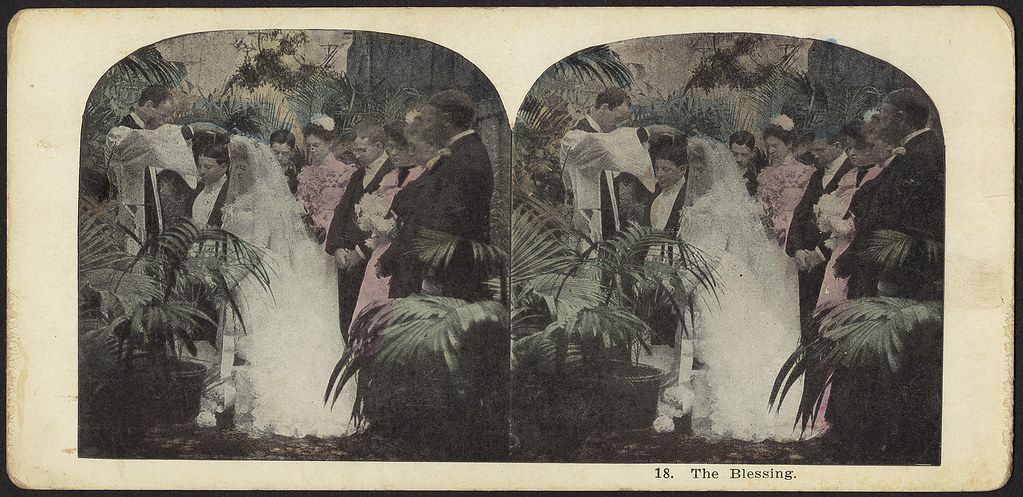 Stereoscope card depicting a wedding ceremony with a bride and groom standing before an altar adorned with palm leaves.