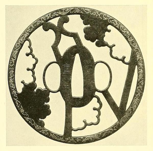 A circular metalwork piece with an intricate, ornate design featuring stylized letters and a repeating pattern of leaves or floral motifs.