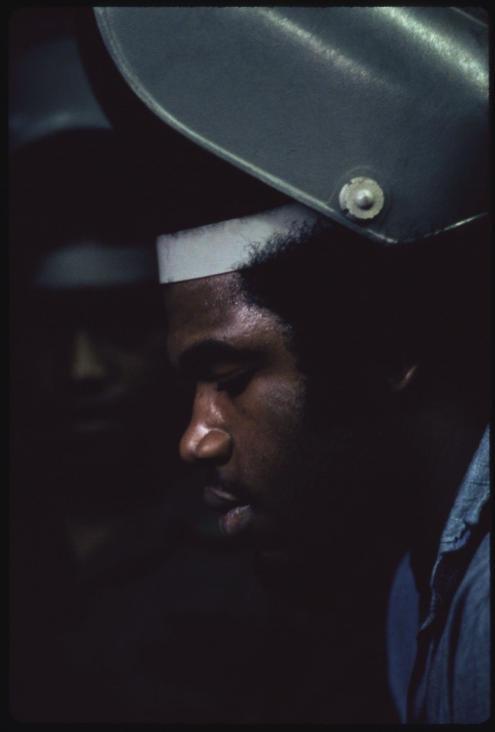 Close-up portrait of a man in uniform, seen in profile with dramatic lighting and strong shadows.