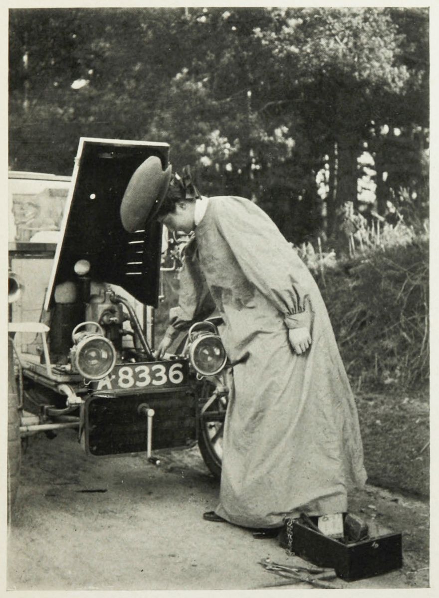 A vintage black and white photograph of a woman working on the engine of a vintage car.