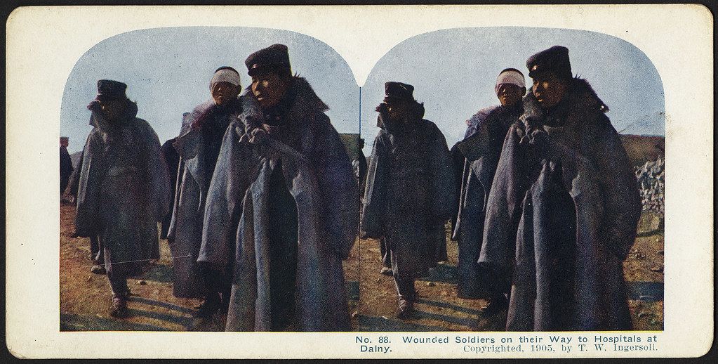 Stereoscopic photograph of wounded soldiers in heavy coats and fur hats walking along a dusty path towards hospitals at Dalny, 1905.