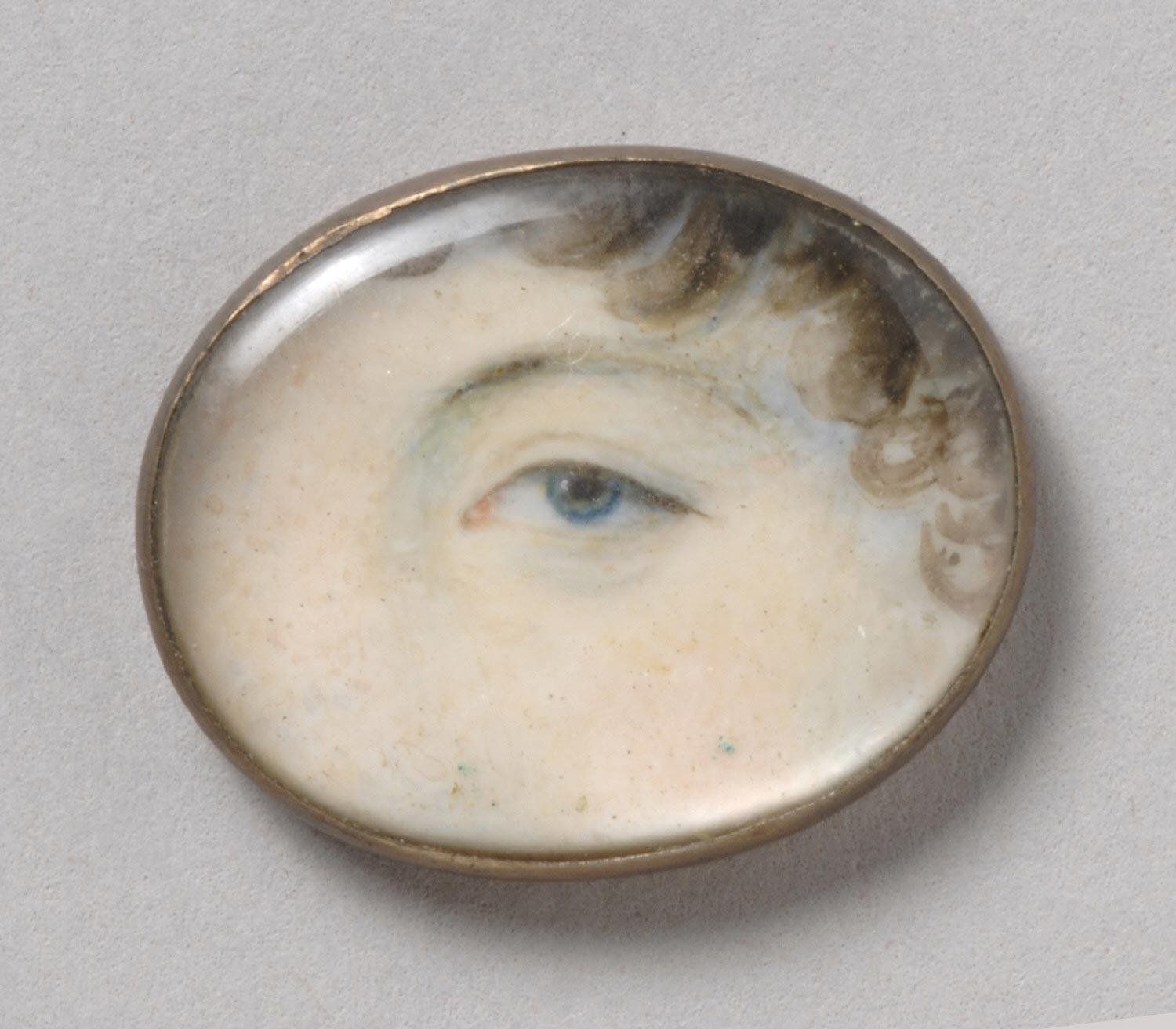 Close-up of a miniature portrait featuring a striking blue eye, encased in a circular brass frame.