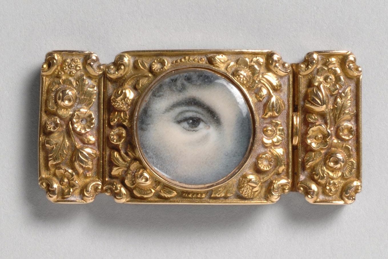 Close-up of a gold brooch with a portrait of an eye in the center.