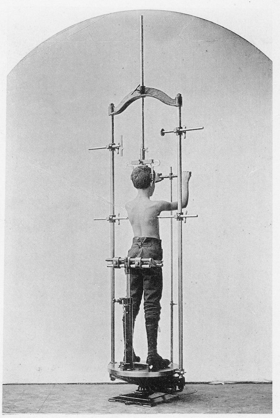 A vintage black and white photograph of a young boy standing within a complex medical device.