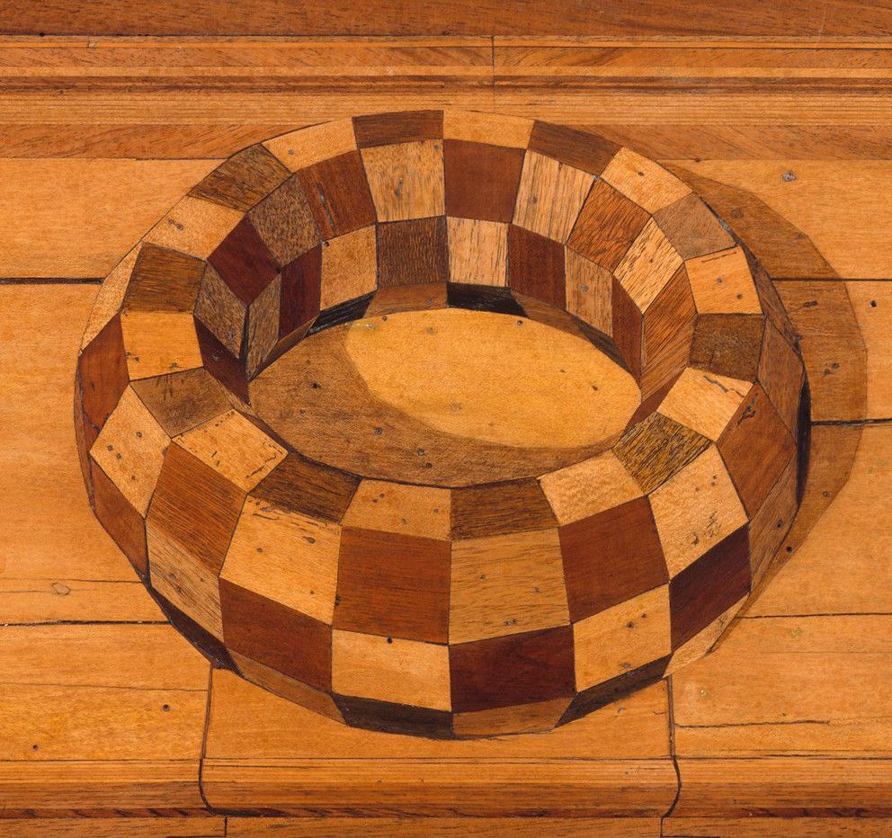 A checkered wooden bowl on a wooden floor.