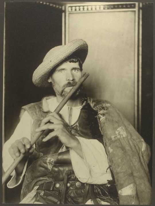 A vintage black and white photograph of a man dressed in a historical costume, playing a flute.