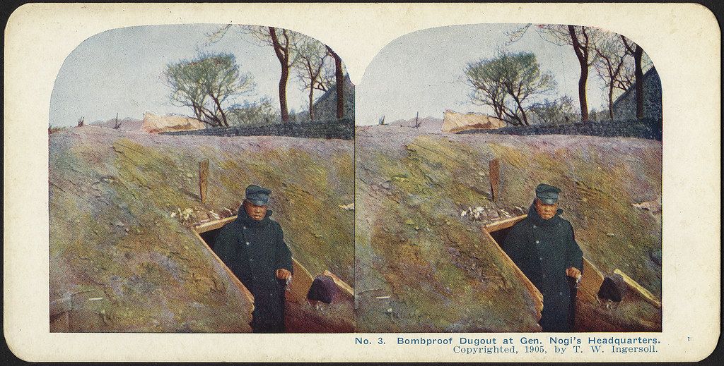 Stereoscopic photograph of a man standing in front of a bombproof dugout at Gen. Nogi's Headquarters in 1905.