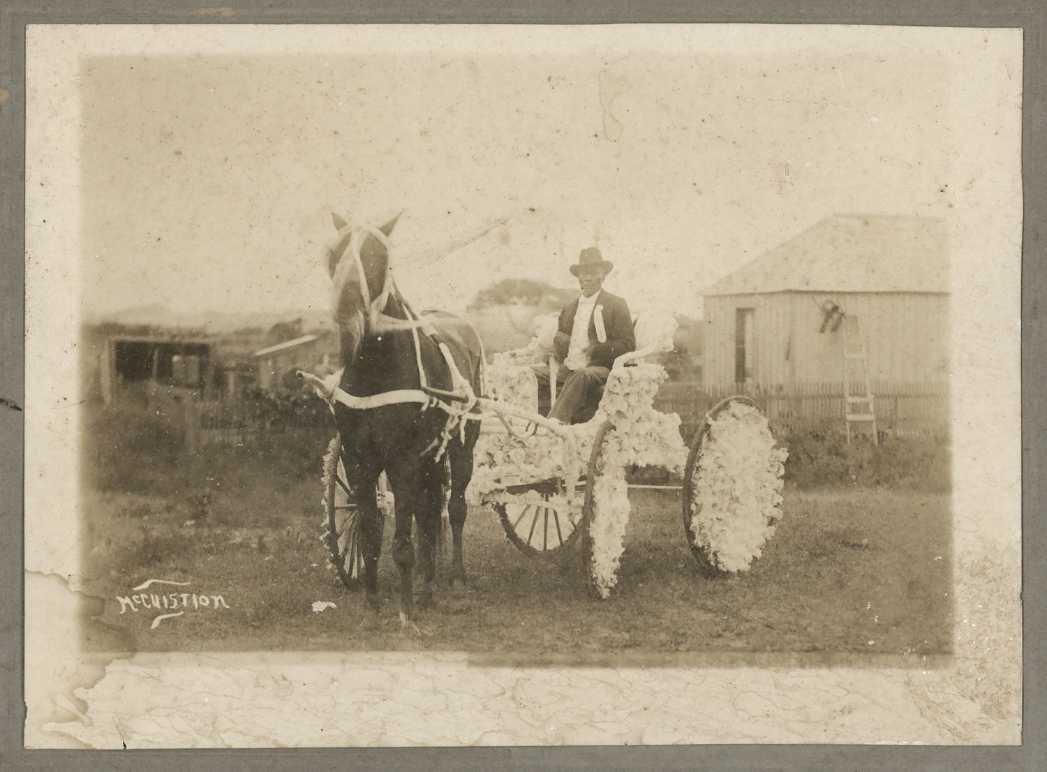 A vintage black and white photograph of a man in a horse-drawn carriage decorated with flowers or cotton.