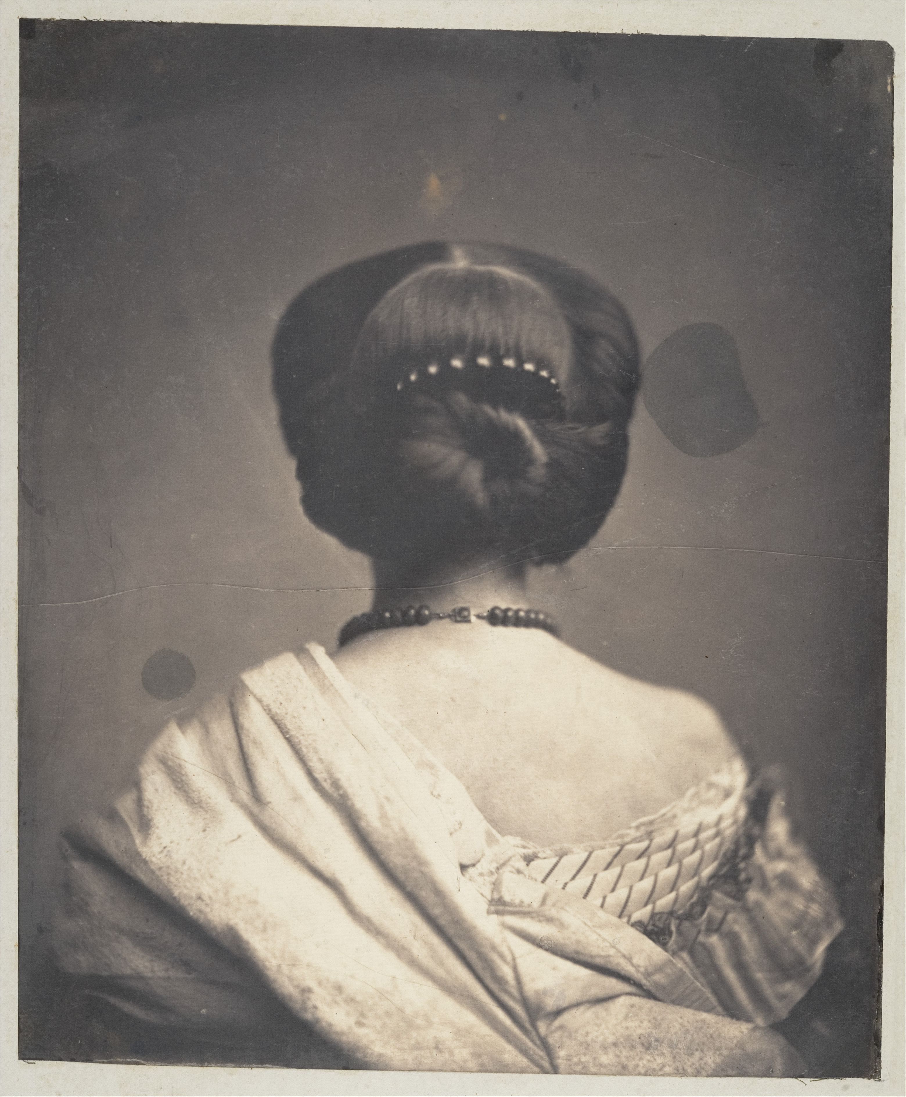 Vintage black and white photograph of a woman from the back, wearing an elaborate updo and a low-cut dress.