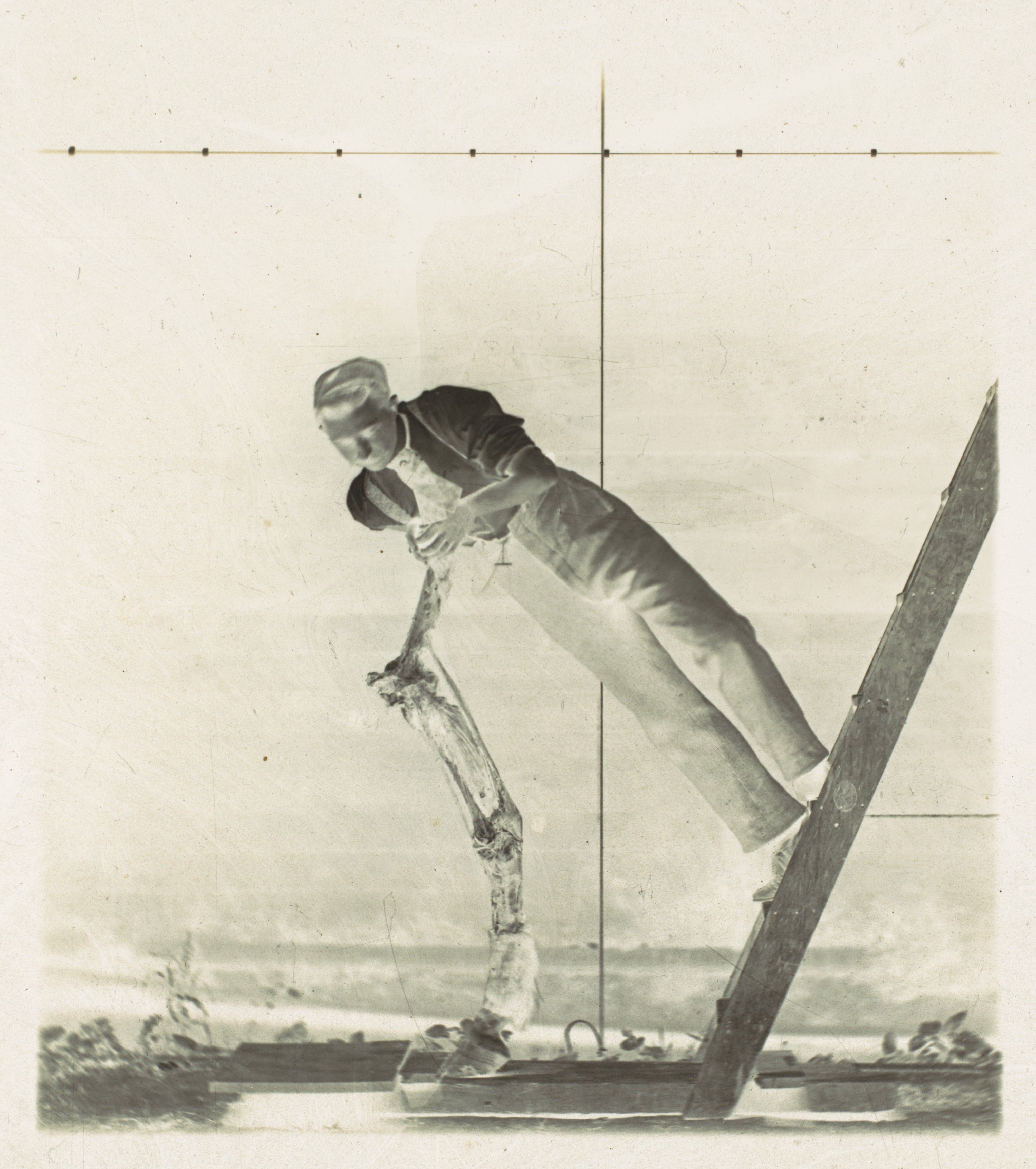 Vintage black and white photograph of a man balancing on a tall wooden pole.