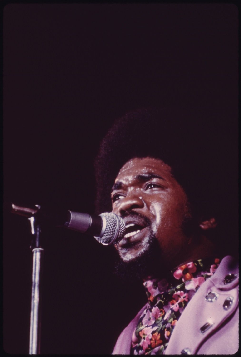 Close-up of a man singing into a microphone on a dark stage.