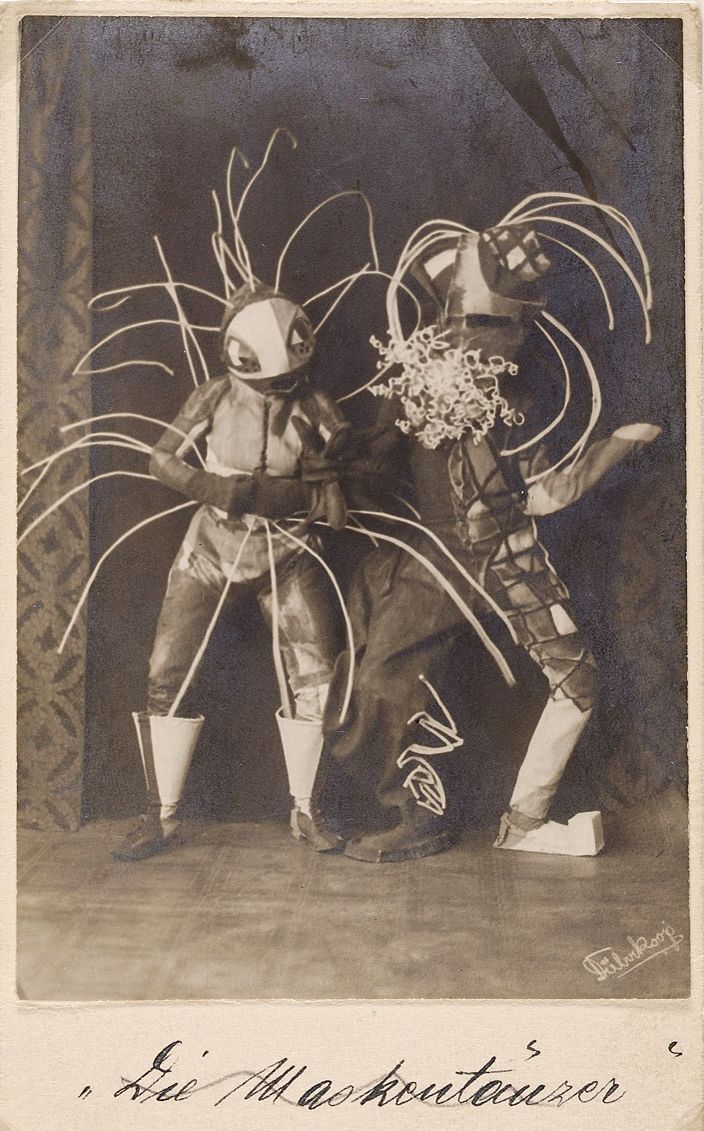A vintage black and white photograph of two performers in elaborate, fantastical costumes on a stage.