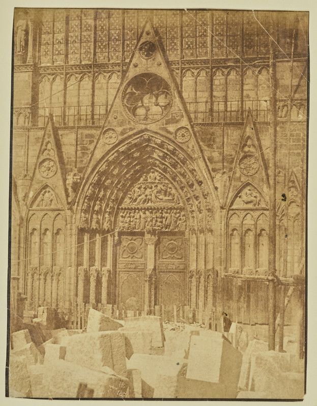 A sepia-toned photograph of a gothic cathedral entrance with a large, pointed archway and intricately carved stone details.