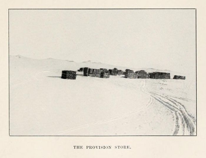 A black and white photograph of a provision store made of stacked wooden crates in a snowy landscape.