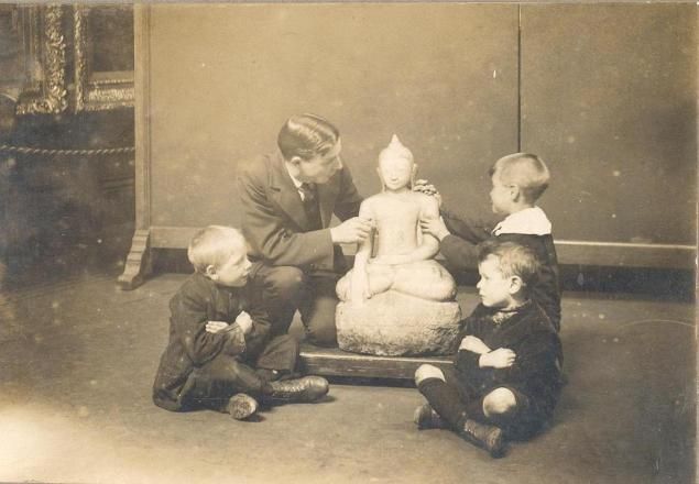 A vintage black and white photograph of a man and four children gathered around a statue.