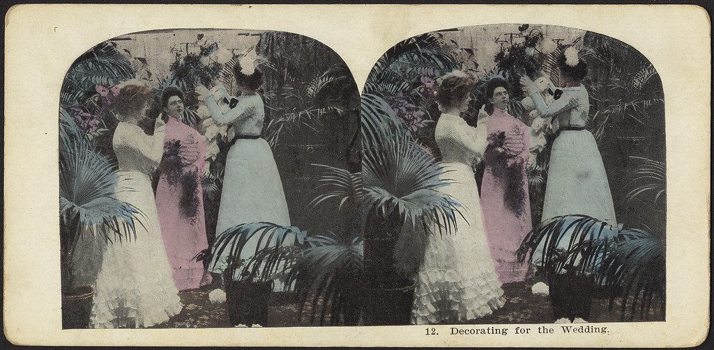 Stereoscopic card depicting four women decorating for a wedding with greenery and flowers in a garden setting.