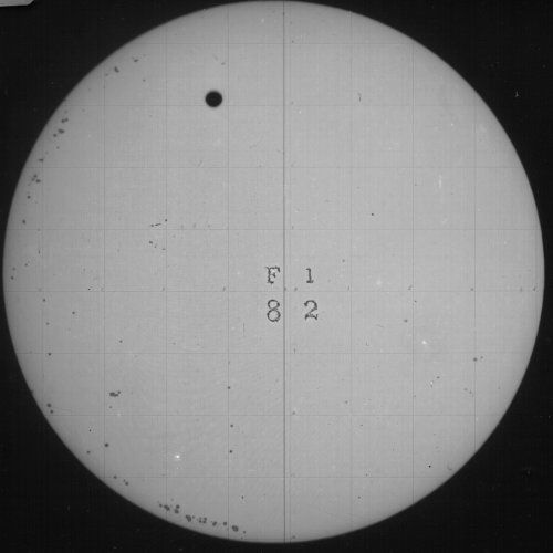 A circular view of the sun with a sunspot and a grid pattern.