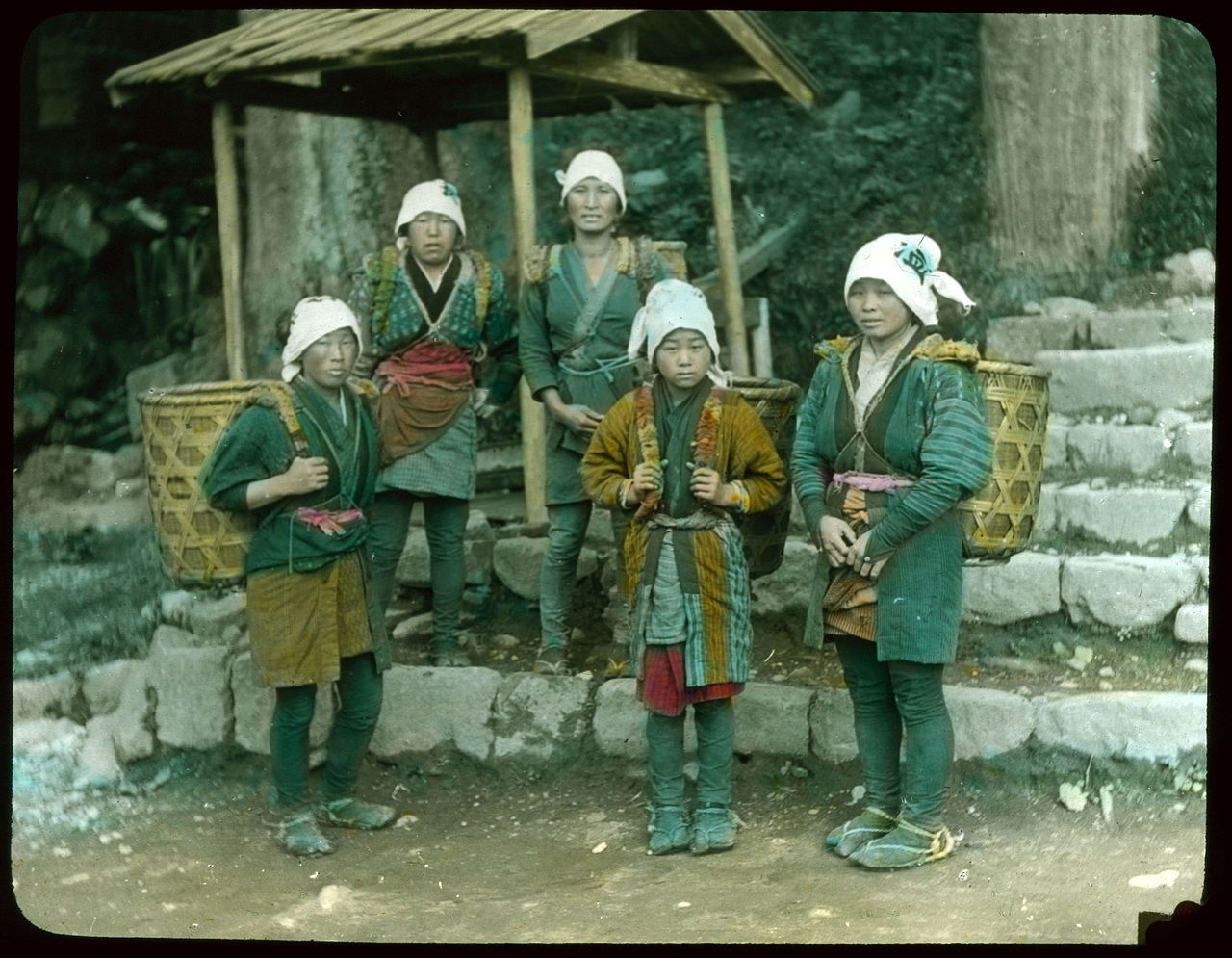 A vintage photograph of five people in traditional Japanese clothing posing in front of a stone staircase and a small wooden structure.