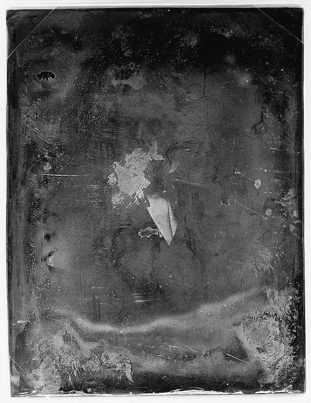 A daguerreotype portrait of a man in a dark suit with a white shirt and bow tie, heavily distressed with scratches and blemishes.