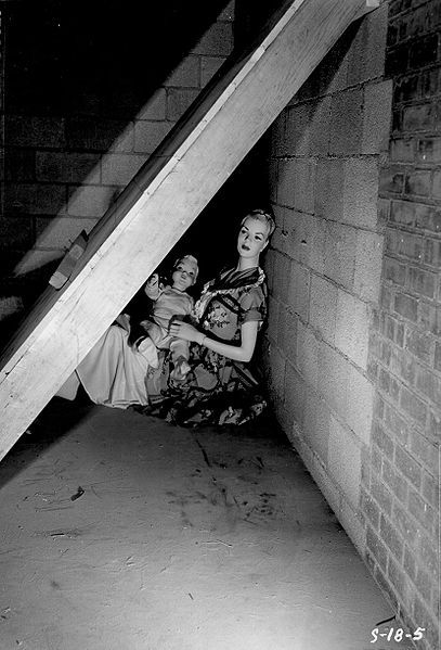 Black and white photograph of a woman and child sitting under a staircase.