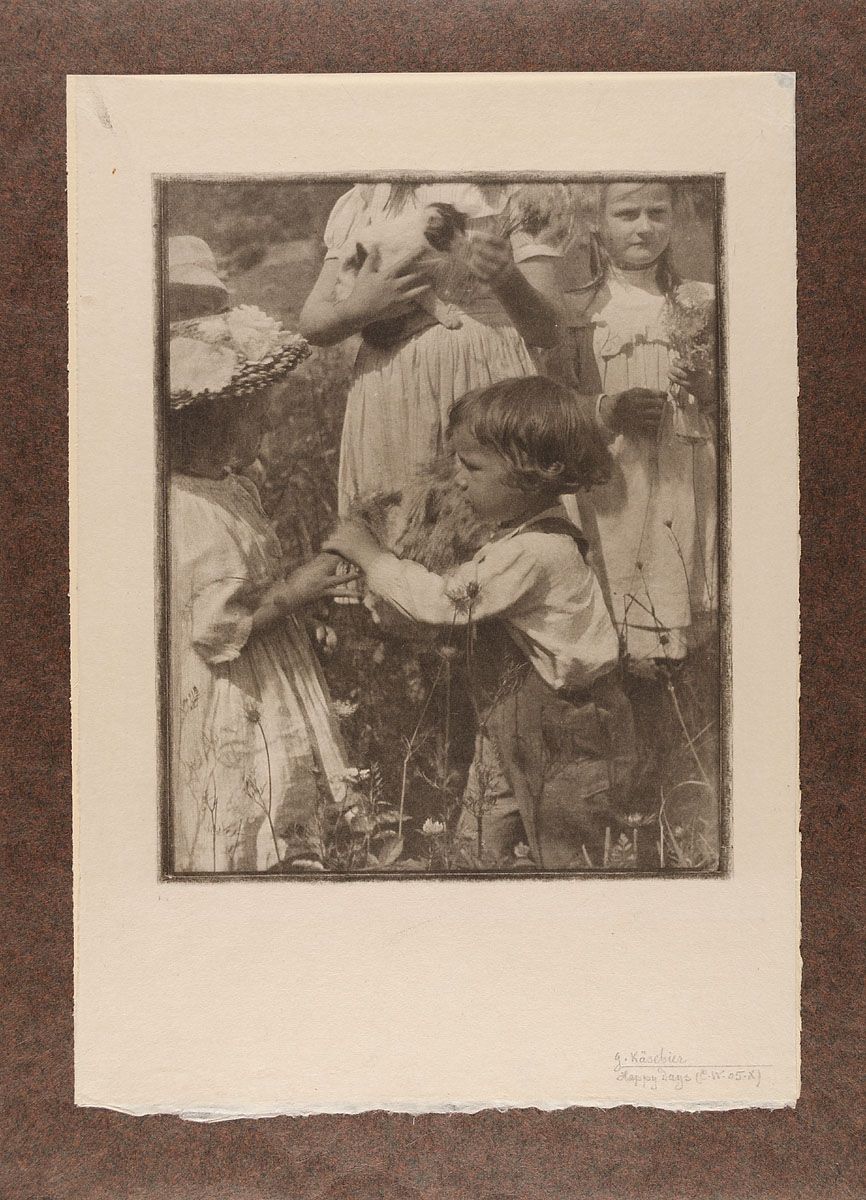 A vintage black and white photograph of a group of children playing in a field of tall grass and wildflowers.