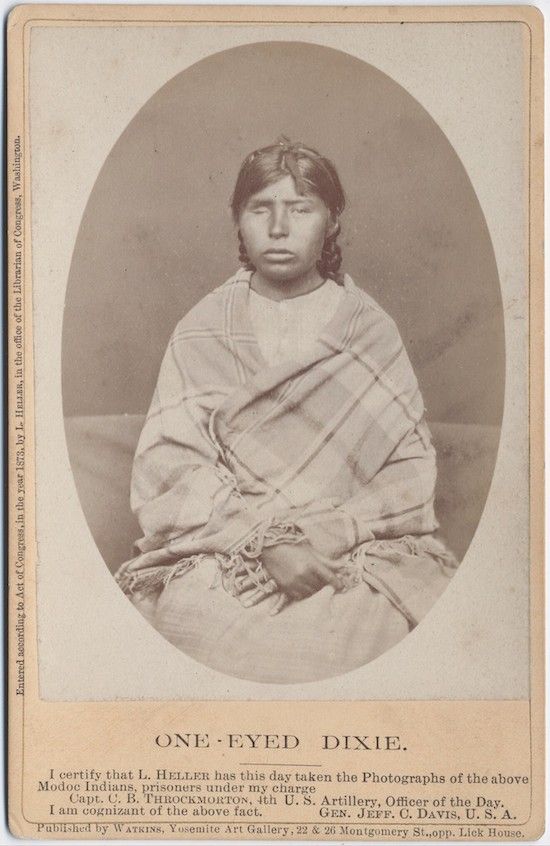 Vintage photograph of One-Eyed Dixie, a Modoc Indian prisoner, seated and wearing patterned clothing and a fringed shawl.