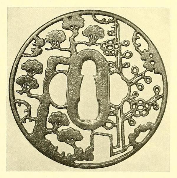 A circular metalwork piece with an intricate, openwork design featuring stylized trees and floral motifs. At the center is a keyhole-shaped opening.