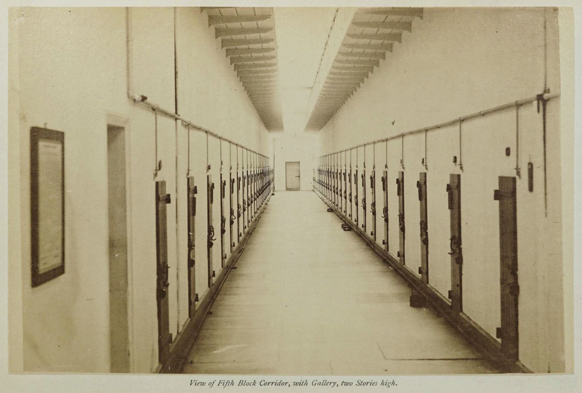 A long, narrow corridor in a prison, lined with two-story cells with metal doors.