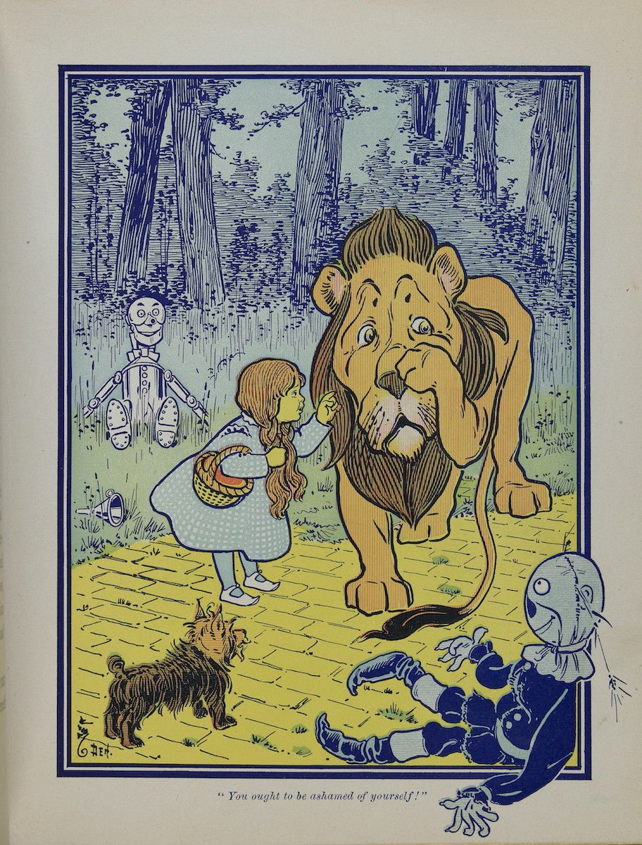 Vintage illustration of Dorothy scolding a crying lion, with the Scarecrow, Tin Woodman, and Toto nearby in a forest setting.